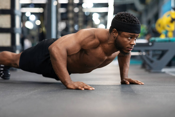 Hemdloser schwarzer Mann macht Liegestütze auf dem Boden im Fitnessstudio - Foto, Bild