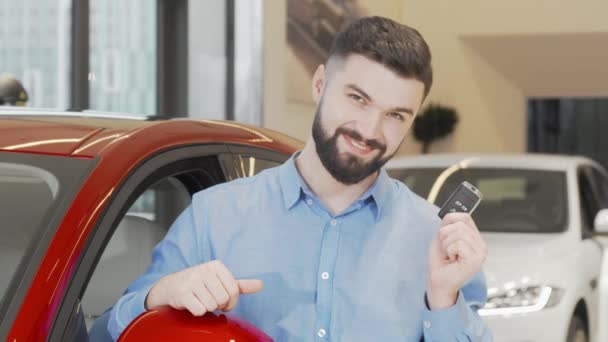 Šťastný atraktivní muž ukazující klíčky od auta do kamery v prodejním salonu - Záběry, video