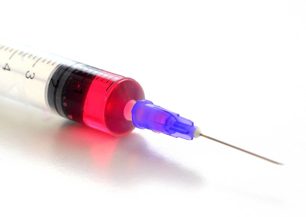 Uma seringa de plástico descartável médica com um medicamento rosa encontra-se em um fundo branco. - Foto, Imagem