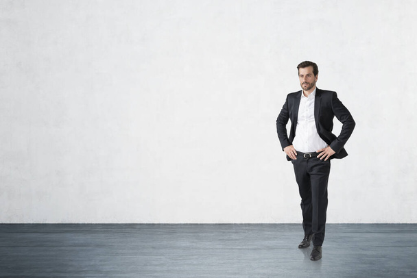 Full length portrait of confident young European businessman standing in concrete wall room. Concept of success. Mock up - Fotografie, Obrázek