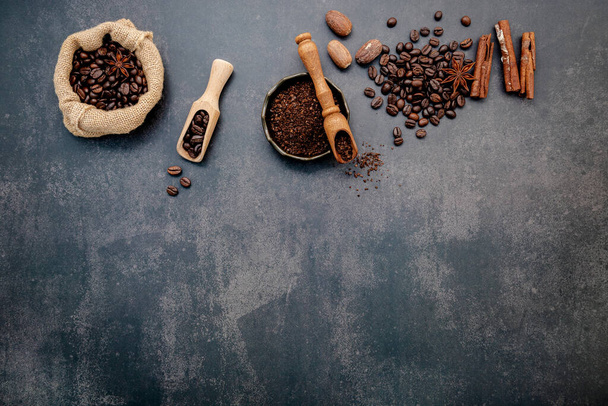 Roasted coffee beans with coffee powder and flavourful ingredients for make tasty coffee setup on dark stone background. - Photo, Image