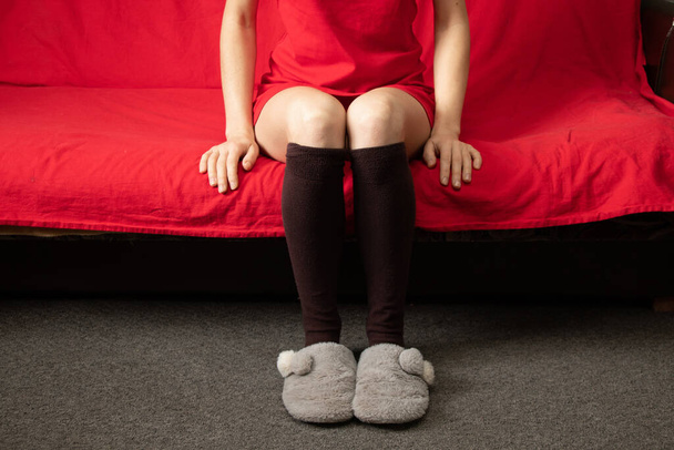 girl sitting in socks and slippers on a red sofa at home on vacation - Фото, зображення