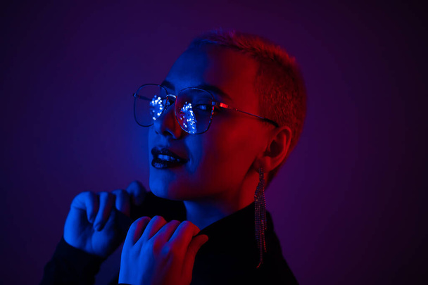 Close-up portrait of young blonde woman with short hair wearing glasses in neon light - Valokuva, kuva