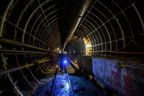 Pracownik z latarnią przechodzi podziemnym tunelem. Budowa linii metra w Dnieprowie, Ukraina. - Zdjęcie, obraz