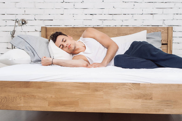 白い枕の上で寝ている男と木製のベッドの上でマットレス。快適な睡眠の概念。整形外科用マットレスと枕 - 写真・画像