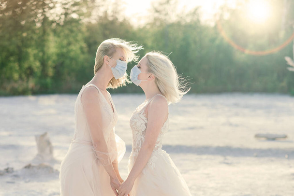 Matrimonio coppia lesbica su sabbia bianca, indossare maschere per prevenire l'epidemia COVID-19 - Foto, immagini