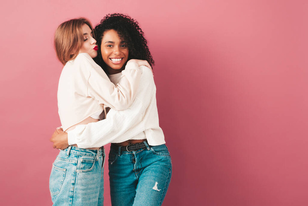 Two young beautiful smiling international hipster female in trendy summer jeans clothes. Sexy carefree women posing near pink wall in studio. Positive models having fun. Concept of friendship  - Foto, Imagen