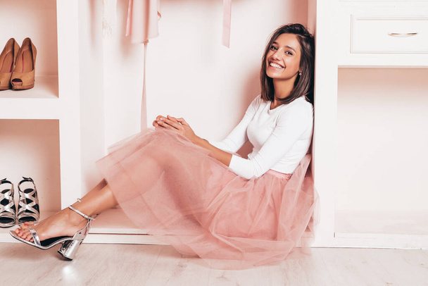 Young beautiful smiling hipster female in trendy summer dress. Sexy carefree woman sitting in pink wardrobe. Positive model having fun. Cheerful and lovely female going crazy - Photo, Image