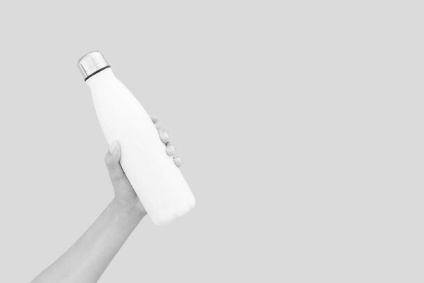 Close-up of female hand holding white reusable steel thermo water bottle isolated on background of grey color with copy space. - Fotó, kép