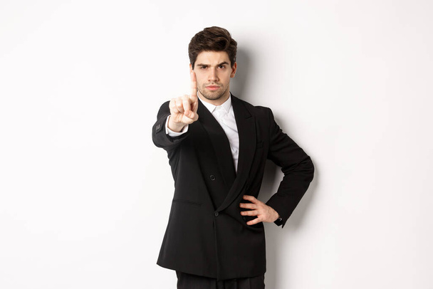 Portret van een knappe man in een zakenpak, met één vinger om iets te verbieden of af te wijzen, te vertellen om te stoppen, het niet met je eens te zijn, over een witte achtergrond te staan - Foto, afbeelding