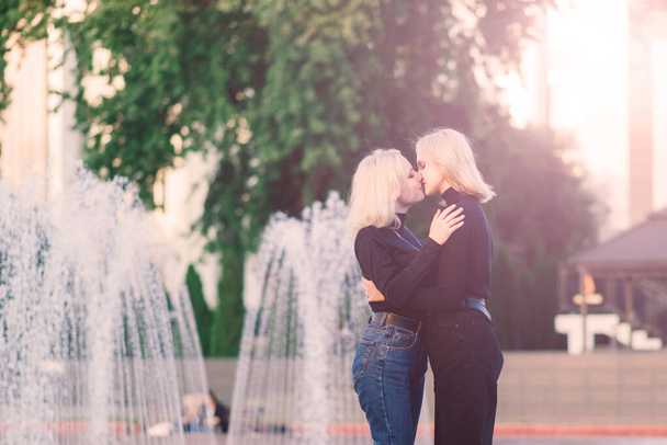 Dos hembras jóvenes caminando sonrientes abrazando y besando al aire libre - Foto, Imagen