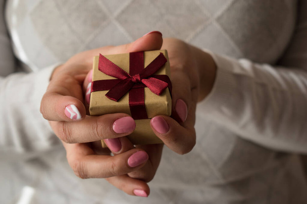 赤いリボンが付いた小さなプレゼントボックスを手に持つ女性の手。バレンタインギフトボックス。女性の手のショットを閉じます.小さなボックスに焦点を当ててフィールドの浅い深さ. - 写真・画像