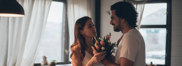 Szerető pár este a nappaliban otthon. Nemzetközi Nőnap. Egy férfi egy csokor tulipánt ad egy nőnek március 8-án. Romantikus családi este otthon. - Fotó, kép