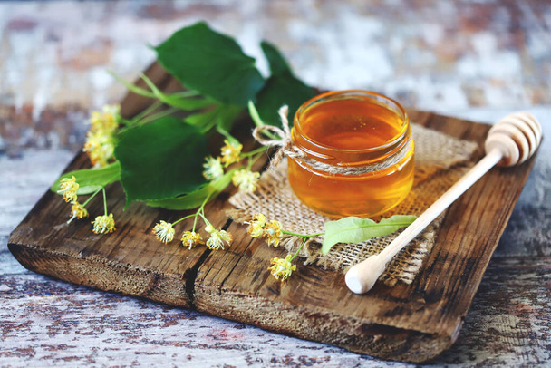 Hou het bij honing met lindehoning. Linden honing in een pot. Bladeren en bloemen van Linden. Zomer verse honing. - Foto, afbeelding