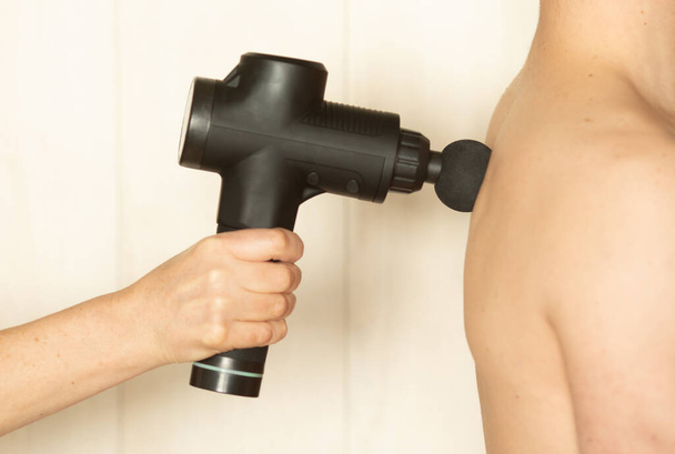 Therapist treating Injury of man. Massage Gun using to massage the body. Sport physical therapy concept. - Foto, afbeelding