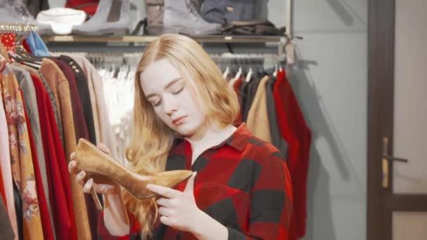 Mujer joven examinando zapatos de tacón alto en la tienda de moda - Imágenes, Vídeo