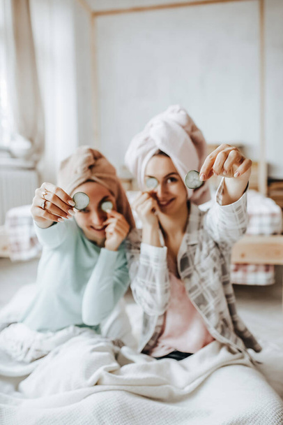 Two girls make homemade face and hair beauty masks. Cucumbers for the freshness of the skin around the eyes. Women take care of youthful skin - Zdjęcie, obraz