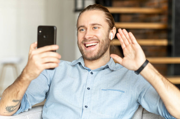 Smiling hipster man waving at mobile phone - Фото, изображение