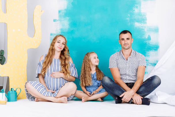 Pregnant family with child girl. Spend time together at home on colorful wall background. A happy family is waiting for the birth of a newborn baby. - Photo, Image