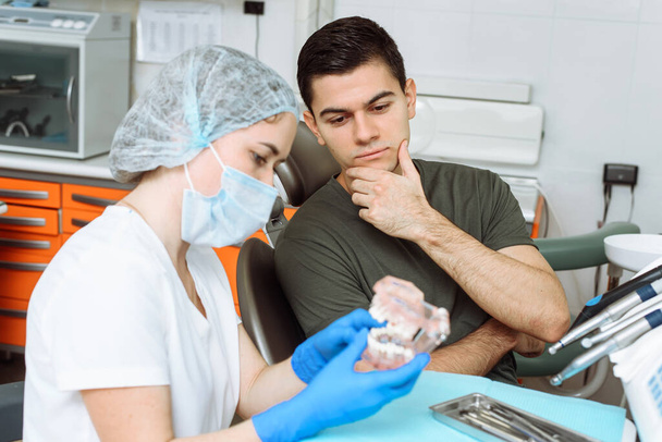 La dentista femminile mostra il trattamento imminente sulla mascella artificiale. Paziente soddisfatto sulla sedia dei dentisti - Foto, immagini