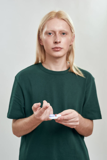 Young caucasian guy holding contact lens on finger - 写真・画像