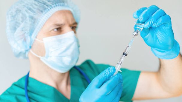 Ein Arzt nimmt Medikamente in Großaufnahme in eine Spritze auf weißem Hintergrund. Coronavirus-Impfstoffstudien. Ein Arzt mit Einmalmaske und Schutzanzug bereitet sich auf eine Injektion und Impfung vor. - Foto, Bild