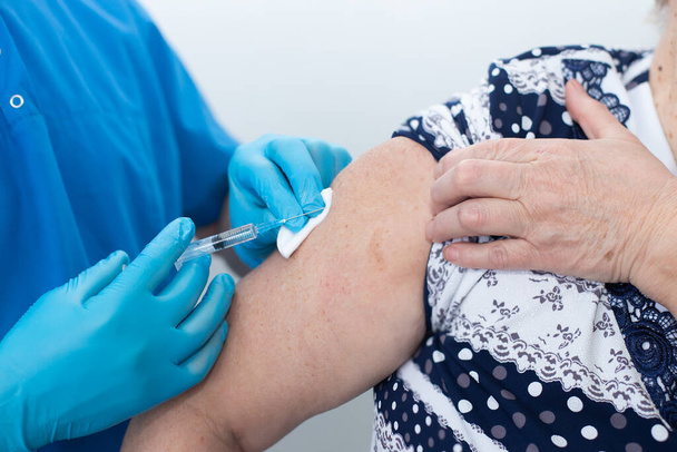 άντρας νοσοκόμος κάνει μια ένεση σε μια ηλικιωμένη γυναίκα, έναν εμβολιασμό - Φωτογραφία, εικόνα