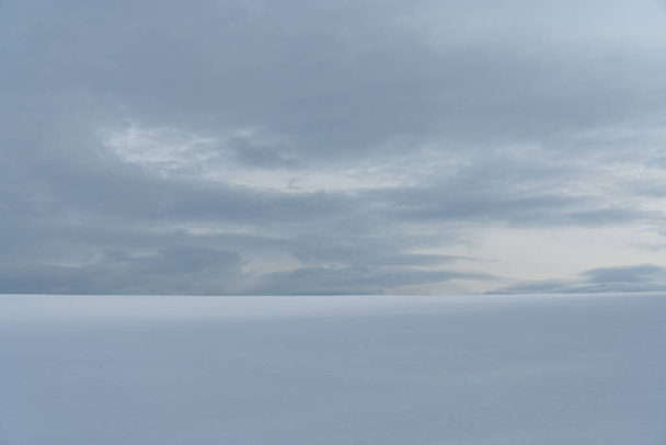 Pohled na zasněžené pole táhnoucí se k obzoru, na jehož konci jsou vidět mraky - Fotografie, Obrázek