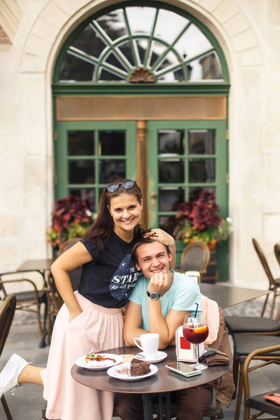 young beautiful couple travelers are sitting at a table in a cafe in the old city of Europe at sunset - Foto, imagen