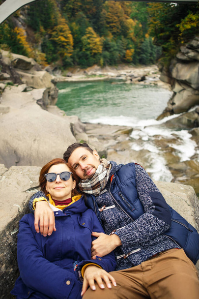 young beautiful couple travelers take a photo on the background of the river and forest - Photo, image