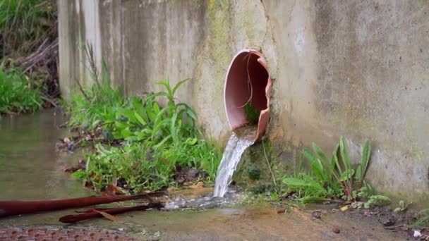 Storm drainage water is drained from the broken plastic pipe onto the grass. Cracked concrete foundation wall. Slow motion - Footage, Video
