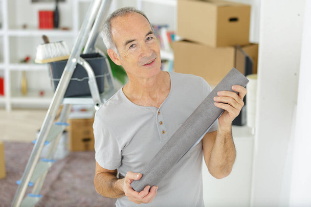 portrait of a senior man holding roll of wallpaper - Фото, изображение
