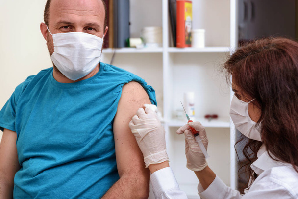 Lékař v rukavicích drží injekční stříkačku a podává pacientovi injekci v lékařské masce. - Fotografie, Obrázek