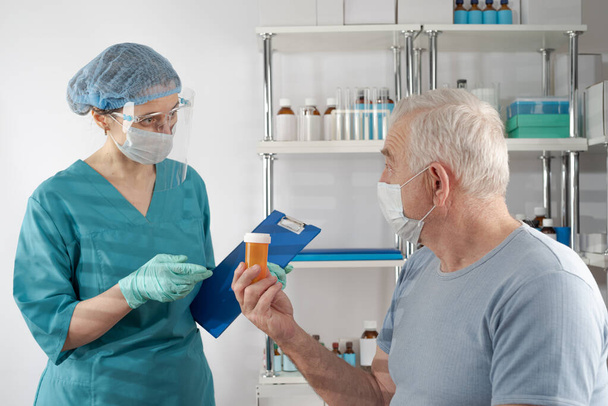 Enfermera sosteniendo una carpeta de portapapeles, dándole un frasco de pastillas naranjas a un adulto mayor. Caso de atención médica del hospital de cita del médico - Foto, imagen