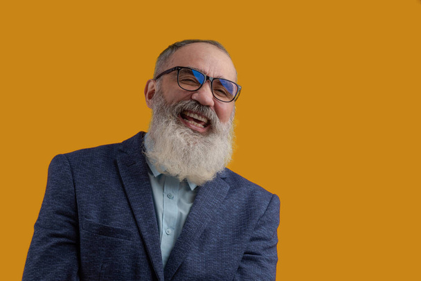 Homme riant charismatique senior avec une barbe grise dans une chemise légère dans une veste décontractée sombre. Fond jaune vif - Photo, image