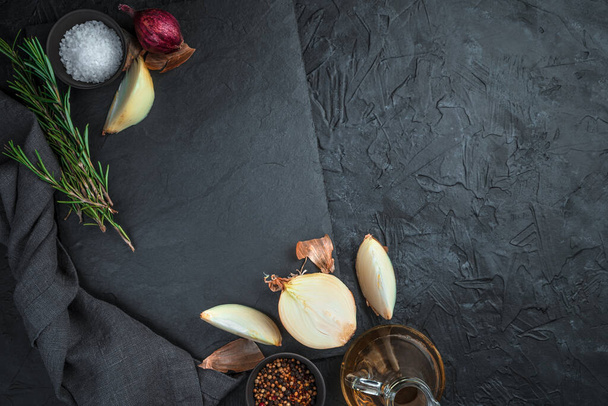 Een lege, platte, rechthoekige schaal, omgeven door uien, specerijen en rozemarijn op een zwarte achtergrond. - Foto, afbeelding
