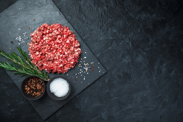 Minced meat, salt, spices and rosemary on a flat tray on a black background. - Photo, image