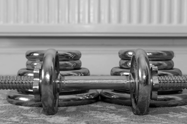 Zwart-wit foto van een kleine halter op de vloer met twee stapels gewichten erachter - Foto, afbeelding