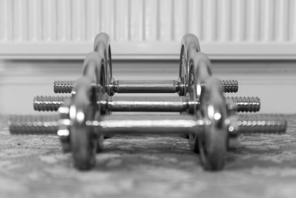 Black and white photo of a row dumbbells on the floor focusing on the heaviest dumbbell in the background - Photo, Image