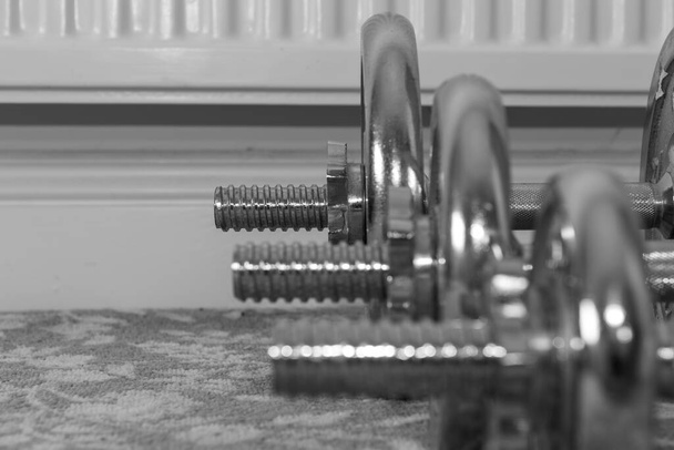 Black and white photo of a row of dumbbells on the floor focusing on the biggest weight in the background - Photo, Image