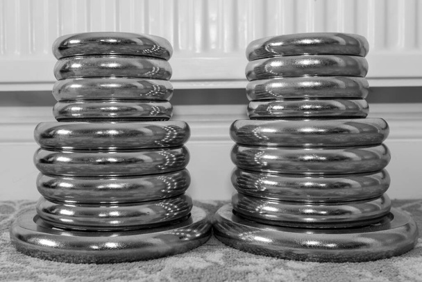 Foto en blanco y negro de dos pilas de pesas de mancuerna en el suelo en casa - Foto, Imagen