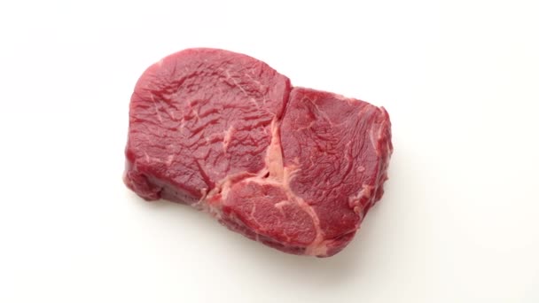 close-up van het draaien van rauw rundvlees steak vlees op witte achtergrond, bovenaanzicht - Video