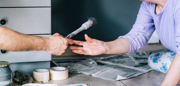 Volwassen stel werkt aan het schilderen van het huis. Handen van een anonieme vrouw en man met een penseel. Verfmuur. DIY Home Decoratie Renovatie. - Foto, afbeelding