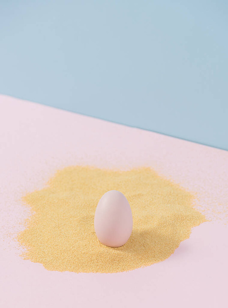 Pastel color egg in sand on powder pink and blue background. Modern Easter card. - Photo, image