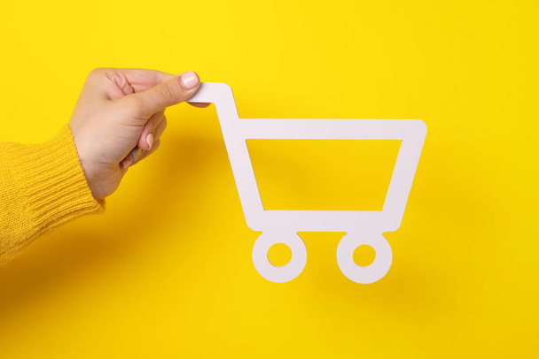 El carrito de la compra en mano femenina sobre fondo amarillo - Foto, Imagen