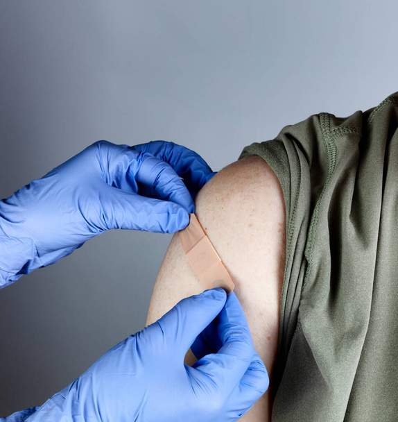 Ιατρός που βάζει επίδεσμο στο ανδρικό άνω μέρος του βραχίονα μετά τη λήψη εμβολίου κατά του ιού.  - Φωτογραφία, εικόνα