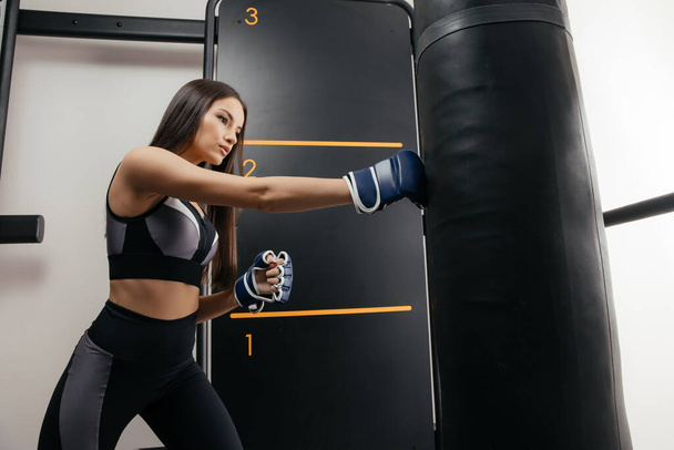 Kaunis 30-vuotias nainen lyö nyrkkeilysäkkiä. Itsepuolustuksen ja suojelun käsite - Valokuva, kuva