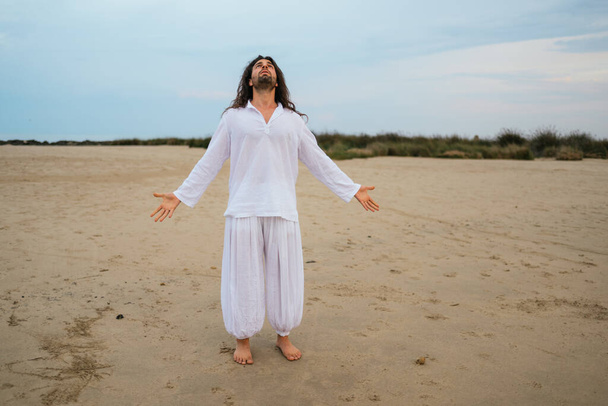 Uzun saçlı yetişkin bir adamın sahilde Tanrı 'yı sorarken çekilmiş resmi.. - Fotoğraf, Görsel