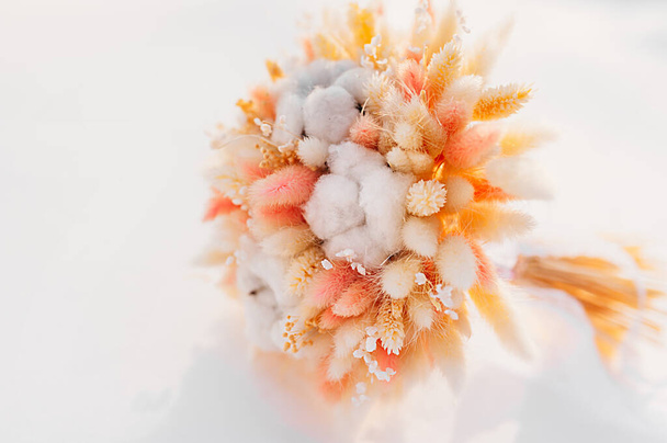 Pfirsichfarbener getrockneter Blumenstrauß aus Getreideähren Baumwolle und Craspedia auf Schnee. sinnvoller Verbrauch natürlicher Materialien, Kommissionierung von Blumensträußen Hobby - Foto, Bild