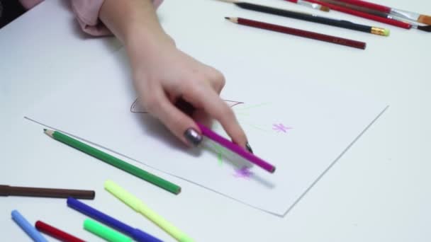 Attraente giovane donna utilizza matite colorate per disegnare un disegno su una carta bianca a tavola - Filmati, video